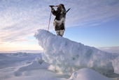 Inuk in furs with telescope looks for seals from ice ridge. Igloolik. Nunavut, Canadian Arctic. 1995