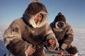 Inuit hunters eating raw fish (arctic char).They wear caribou skin clothes. Igloolik, Nunavut, Canada. 1990