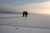Two inuit hunters walk to the edge of the fast ice leaving footprints. Baffin Is. Nunavut, Canada. 1990