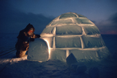 Tatigat,an inuk, pulls aside the snow brick over the igloo door at dusk. Igloolik. Nunavut. Canada. 1993
