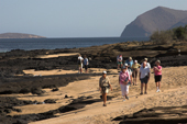 Visitors on the lava and sand shoreline at Puerto Egas, Santiago, Galapagos. Ecuador.