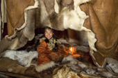 Nadia Takui, a Chukchi girl, dressed in a traditional reindeer skin Kerker, (knee length coverall), sitting at the edge of the polog (sleeping area) in a Yaranga (tent) at a reindeer herders' summer camp. Iultinsky District, Chukotka, Siberia, Russia