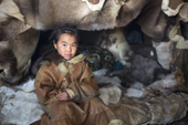 Nadia Takui, a Chukchi girl, dressed in a traditional reindeer skin Kamleika (parka), sits by the by the front of the polog (sleeping area) in a Yaranga (tent) at a reindeer herders' summer camp. Iultinsky District, Chukotka, Siberia, Russia