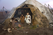 Yarosalva & Nadia, two Chukchi girls, stand by the entrance of a Yaranga (tent) while Tamara, Nadia's mother, tends a ritual fire at the start of the Chukchi 'Festival of the Young Reindeer' at a herders' summer camp. Iultinsky District, Chukotka, Siberia, Russia.