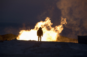 At dusk, a geologist stands in front of a gas flare at a drilling site in the South Tambey gas field. Yamal Peninsula, NW Siberia, Russia
