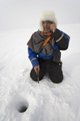 Saami reindeer herder, Nils Peder Gaup, chats on his mobile phone while ice fishing for Arctic Char on a lake near his reindeers' winter pastures. Kautokeino, Finnmark, North Norway. 2007