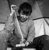 Magssanguak Imina making a traditional string puzzle that represents a tent, while sitting in a tent. Thule, Northwest Greenland. 1971