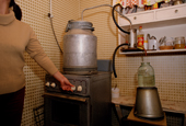 A Russian woman making 'Samagon' (homebrewed vodka) on a stove in the kitchen of a Moscow apartment. Russia.