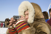 A Nenets spectator uses his mobile phone to photograph a reindeer race at a herders festival in the Yamal. Western Siberia, Russia